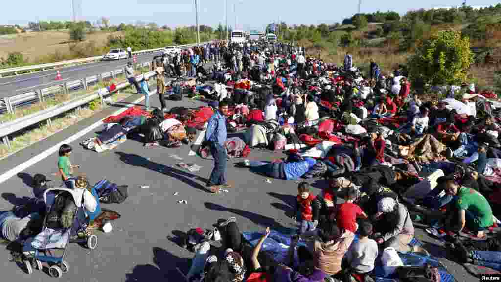 Plusieurs hommes, femmes et enfants manifestent sur une autoroute bloquée par des policiers et des gendarmes turques qui font barrage à des centaines de migrants principalement syriens près d’Edirne, en Turquie, 19 septembre 2015. 