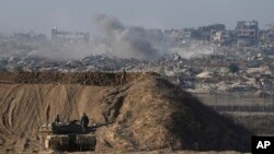Un soldat israélien regarde une partie détruite de la ville de Gaza tandis que d'autres se tiennent sur un véhicule blindé à la frontière entre Israël et Gaza, vue du sud d'Israël, le 1er décembre 2024. (AP Photo/Tsafrir Abayov)