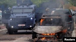 Agentes de las fuerzas policiales de Kosovo actúan en medio de enfrentamientos con manifestantes de la población serbia en esa nación, mientras un automóvil se incinera, en el pueblo de Zvecan, el viernes 26 de mayo de 2023.