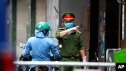 A police officer talks to a woman at the barricaded entrance of an alley where one of its residents is suspected to have COVID-19 in Hanoi, Vietnam on Wednesday, July 29, 2020. Vietnam intensifies protective measures as the number of locally…