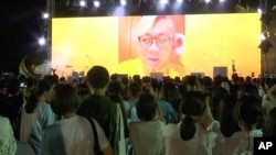 In this image taken from video, Pavin Chachavalpongpun, administrator of the Facebook group “Royalist Marketplace,” is shown delivering a pre-recorded message onscreen before a crowd attending an anti-government rally on Aug. 10, 2020, at Thammasat Univer