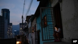Una mujer mira su teléfono inteligente afuera de su casa en el barrio San Agustín de Caracas. Mayo 17, 2020.