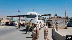 Pasukan pemerintah Suriah mengawasi evakuasi dengan bus pejuang Angkatan Darat Islam dari kota terkepung Douma, sebelah timur Damaskus, Suriah, 2 April 2018. (Foto: SANA via AP)