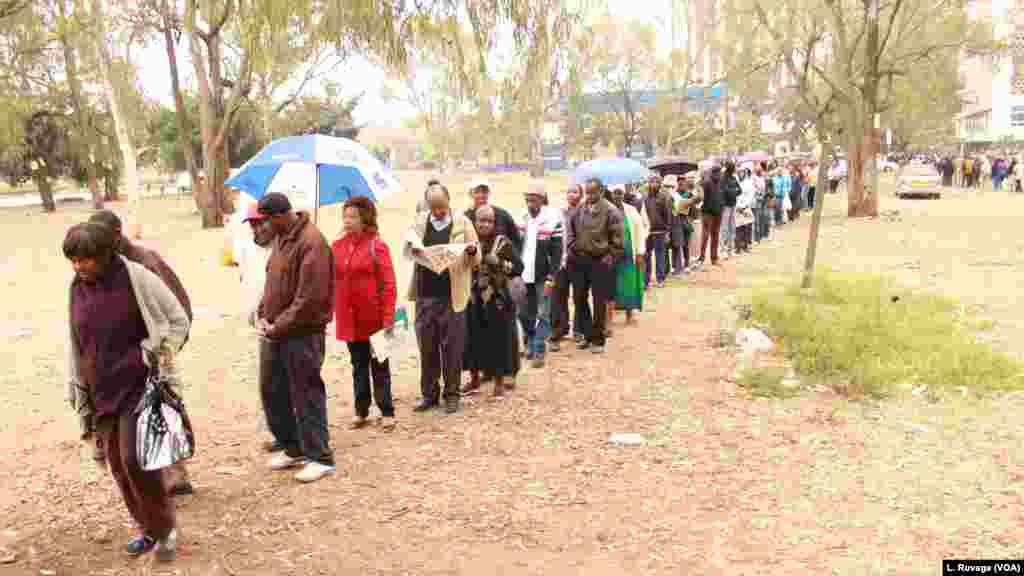A Kenyan voter catches up with the day's news as he waits in line with others to cast his ballot. (L. Ruvaga/VOA)