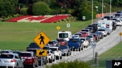Una fila de vehículos espera para ingresar a Canadá en el cruce fronterizo de Peace Arch, a la vista de una bandera canadiense hecha de flores, el 9 de agosto de 2021, en Blaine, EE. UU.
