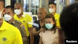 Sararat Rangsiwuthaporn, a suspect in over a dozen murders, is escorted by police officers at a police station in Bangkok