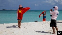 FILE - Chinese tourists take souvenir photos with the Chinese national flag as they visit Quanfu Island, one of Paracel Islands of Sansha prefecture of southern China's Hainan province in the South China Sea, Sept. 14, 2014. 