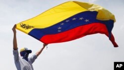 ARCHIVO - Un manifestante antigubernamental enmascarado ondea una bandera venezolana durante las protestas en Caracas, Venezuela, el 1 de mayo de 2019.