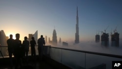 FILE - Photographers take pictures as the sun rises over the city skyline with the Burj Khalifa, world's tallest building at the backdrop, seen from a balcony on the 42nd floor of a hotel on a foggy day in Dubai, United Arab Emirates, Dec. 31, 2016. (AP Photo/Kamran Jebreili)