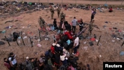 Migrantes intentan cruzar una valla de alambre de púas desplegada para impedir el cruce de migrantes a EEUU, a orillas del río Bravo, en la frontera con México, visto desde Piedras Negras, Coahuila, el 21 de diciembre de 2023.