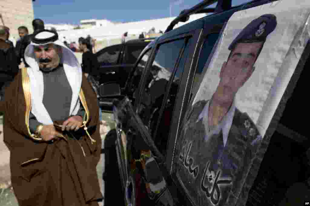 A Jordanian man walks past a poster that is pasted on a vehicle with a picture of slain Jordanian pilot, Lt. Muath al-Kaseasbeh with Arabic that reads, "We are all Muath," at his home village of Ai, near Karak, Feb. 4, 2015.