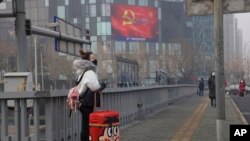 A traveler stands on a bridge near a display showing government propaganda in the fight against the COVID-19 viral illness in Beijing, China, Feb. 13, 2020.