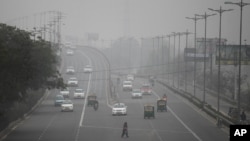 FILE - An Indian woman crosses a road as vehicles move through morning smog on the last day of a two-week experiment to reduce the number of cars to fight pollution in New Delhi, Jan. 15, 2016. 