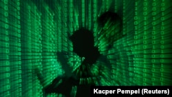 Foto ilustrasi memperlihatkan kode biner diproyeksikan pada seorang pria yang memegang komputer laptop, di sebuah kantor di Warsawa (foto: dok).