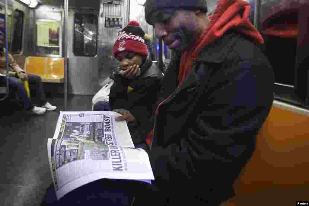 Daniel Mitchell berbicara dengan anaknya Daniel Mitchell II tentang kematian dua polisi yang ditembak sampai tewas di Brooklyn, ketika mereka membaca surat kabar lokal di kereta G di New York, 22 Desember 2014.
