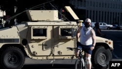 Un hombre en bicicleta pasa frente a un vehículo blindado de la Guardia Nacional cerca de la Casa Blanca, el lunes 1 de junio de 2020, cuando manifestantes se reúnen para protestar la muerte del afroestadounidense George Floyd en custodia policial.