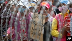 Cambodian garment workers shout slogans behind barbed wire set up by police near the Council of Ministers building during a rally in Phnom Penh, Cambodia, Monday, Dec. 30, 2013. The workers are demanding a raise in their monthly salary from US $160 to $80. (AP Photo/Heng Sinith)