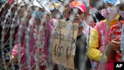 Cambodian garment workers shout slogans behind barbed wire set up by police near the Council of Ministers building during a rally in Phnom Penh, Cambodia, Monday, Dec. 30, 2013. The workers are demanding a raise in their monthly salary from US $160 to $80. (AP Photo/Heng Sinith)
