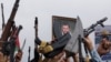FILE - A poster of Houthi leader Abdul-Malek al-Houthi is held by a protester as others hold up their weapons during a rally to show support to Palestinians in the Gaza Strip, amid the Israel-Hamas conflict, in Sanaa, Yemen, July 26, 2024. 