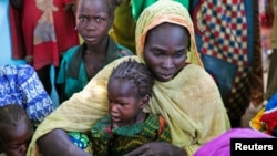 FILE - A mother and her child sit with other families at a camp for internally displaced people in Dougi, Cameroon. 