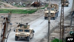Vehicles belonging to the US-led coalition drive down a street in the front line Syrian village of Baghuz, Feb. 17, 2019. 