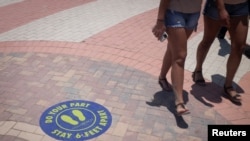 Bañistas caminan junto a una señal en el piso que indica mantener el distanciamiento social para evitar el contagio de coronavirus en Miami Beach, Florida. Junio 10, 2020.