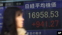 Seorang perempuan berjalan melewati papan elektronik di depan perusahaan sekuritas di Tokyo, Jepang (22/1). 
