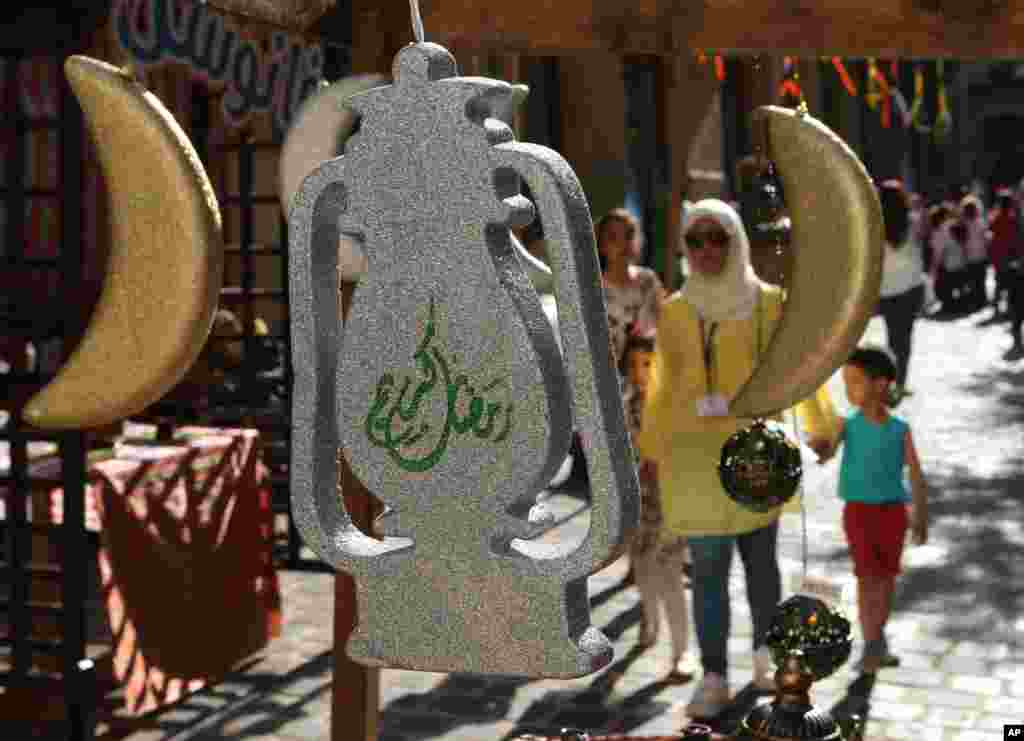 Seorang perempuan Lebanon dan anak-anaknya berjalan melewati aneka hiasan lentera dan bulan sabit khas Ramadan, di pusat kota Beirut (14/6). (AP Photo/Hussein Malla)
