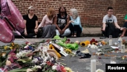 Women sit by an impromptu memorial of flowers commemorating the victims at the scene of the car attack on a group of counterprotesters during the "Unite the Right" rally as people continue to react to the weekend violence in Charlottesville, Va., Aug. 14,