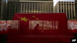 资料照：香港主权移交26周年纪念期间，中国国旗和香港区旗高挂香港街道大楼，旗帜后有行人走过天桥。（美联社，2023年6月27日）