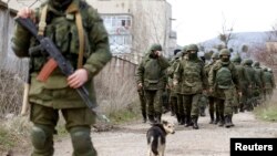 Para pria bersenjata diyakini sebagai orang-orang Rusia berjalan di luar pangkalan militer Ukraina di Perevalnoye, dekat Krimea (14/3).