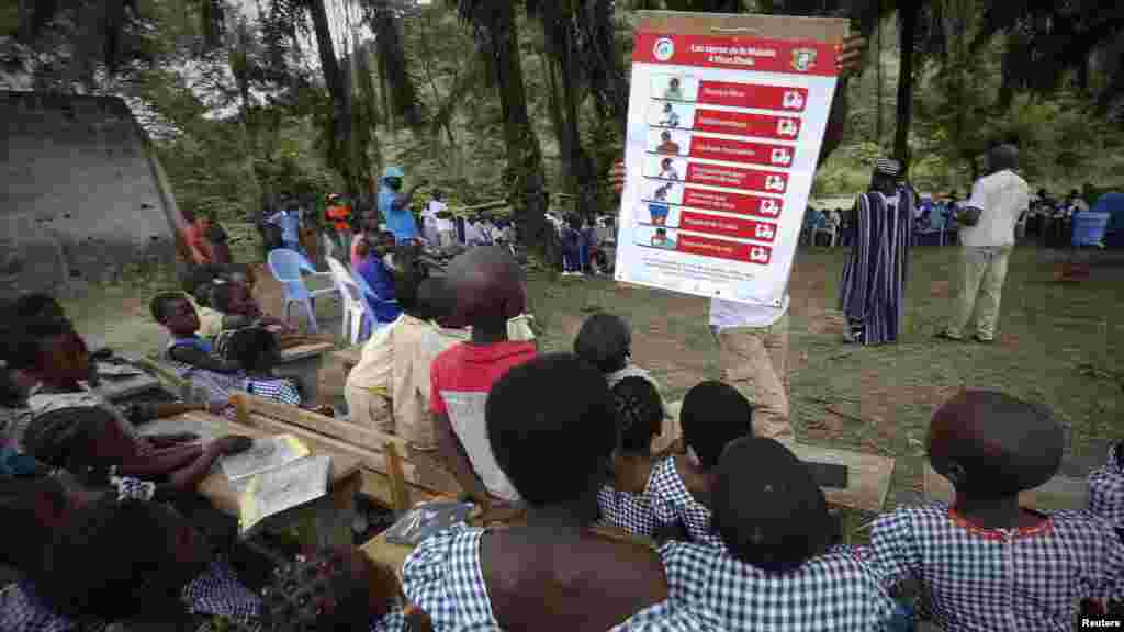 A man shows students a poster on the symptoms of Ebola during a United Nations Children's Fund (UNICEF) Ebola awareness drive in Gueupleu, Man, western Ivory Coast, Nov. 3, 2014.