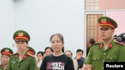 អ្នកស្រី Nguyen Ngoc Nhu Quynh (រូប​កណ្តាល) ដែល​ជា​អ្នក​សរសេរ​ប្លុក​ដ៏​ល្បី​មួយ​រូប​ឈរ​នៅ​ចម្លោះ​ប៉ូលិស​នៅ​ក្នុង​សវនាការ​របស់​អ្នកស្រី​នៅ​ក្នុង​ក្រុង Nha Trang ប្រទេស​វៀតណាម កាលពី​ថ្ងៃទី៣០ ខែវិច្ឆិកា ឆ្នាំ២០១៧។