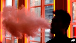FILE - In this Feb. 20, 2014 file photo, a customer exhales vapor from an e-cigarette at a store in New York. A growing number of e-cigarette and vaporizer sellers have started offering college scholarships as a way to get their brands listed on university websites.