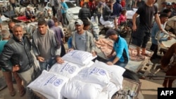 Ljudi pune svoja kolica vrećama brašna u distributivnom centru UNRWA u Deir el-Balahu u centralnom pojasu Gaze, 3. novembar, 2024.(Foto: AFP /Eyad BABA)
