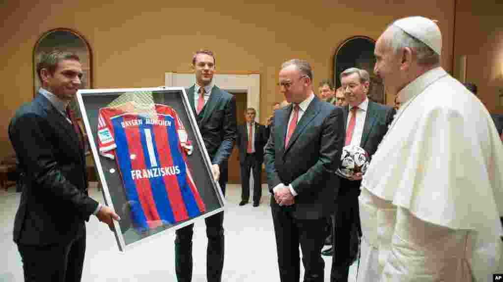 Sur cette photo fournie par le journal du Vatican L'Osservatore Romano, le capitaine de l'équipe Bayern, Philipp Lahm, à gauche, et le gardien Manuel Neuer présentent un maillot du Bayern au pape François lors d'une audience privée avec l'équipe et les responsables au Vatican, mercredi,