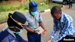 Un policier montre à un visiteur comment désinfecter ses mains contre la propagation de la maladie à coronavirus au palais présidentiel à Harare, Zimbabwe, le 19 mars 2020. (REUTERS/Philimon Bulawayo)