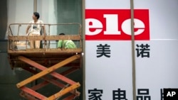 Workers ride a scissor lift as they install banners for the grand opening of a home electronics store in Beijing, Wednesday, July 15, 2015.