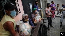 Residentes ayudan a descargar bolsas de alimentos básicos, como pasta, azúcar, harina y aceite de cocina, proporcionados por un programa de asistencia alimentaria del gobierno, en el barrio Santa Rosalía de Caracas, Venezuela, el sábado 10 de abril 2021.