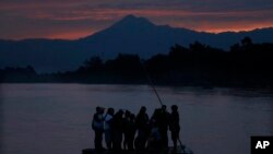 Central American migrants stand on a raft to cross the Suchiate River from Guatemala to Mexico, as the Tacana volcano stands tall near Ciudad Hidalgo, Mexico, early Monday, June 10, 2019.