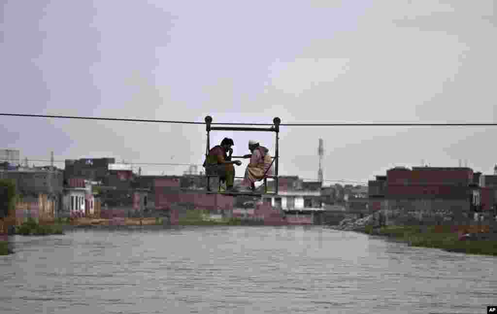 Dua orang Pakistan ngobrol sambil menyeberangi sungai, menggunakan 'jembatan' yang dioperasikan dengan tali di pinggiran Islamabad.