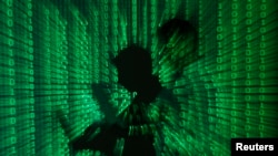 Illustration shows projection of binary code on a man holding a laptop computer, in an office.