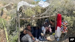 Migrantes colombianos se reúnen en una sombra hecha por ellos mismos mientras esperan ser procesados por los agentes de la Patrulla Fronteriza de Estados Unidos cerca de Jacumba Hot Springs, en el sureste del condado de San Diego, California, el sábado 13 de mayo de 2023.