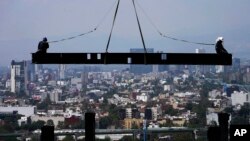 ARCHIVO - Trabajadores de la construcción viajan sobre una viga que cuelga de una grúa en el sitio de construcción de un edificio residencial de gran altura en la Ciudad de México, 17 de junio de 2022. 