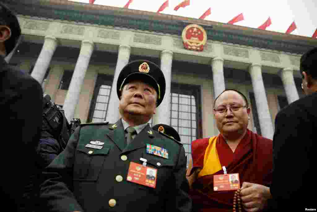 2018年3月3日，在北京参加中国人民政治协商会议的一位军人代表和一位穿着喇嘛服装、手拿念珠的代表在开幕式结束后离开人民大会堂。