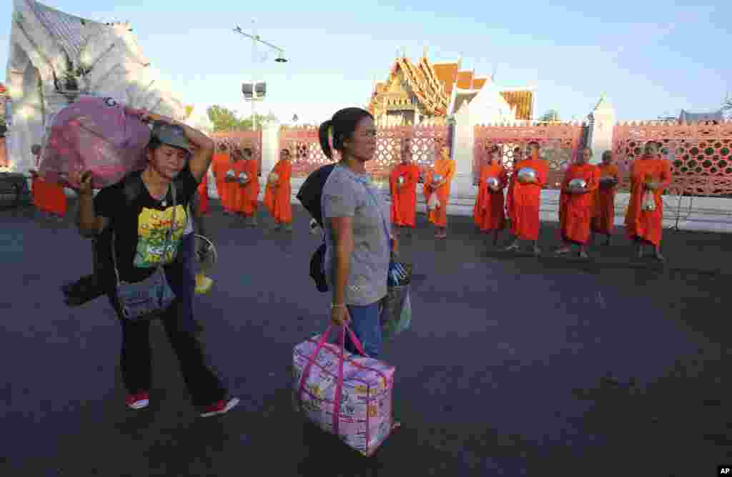 Anti-government demonstrators leave a demonstration site with their belongings, walking past Buddhist monks a day after military soldiers staged a coup, in Bangkok, May 23, 2014.