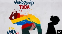 Una mujer vende frutas frente a un mural con el mapa de Venezuela donde se promueve la participación pro oficialista en el referendo consultivo del domingo, en Caracas, el 29 de noviembre de 2023.