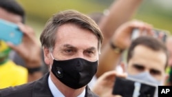 El presidente de Brasil, Jair Bolsonaro, se encuentra en medio de partidarios que toman fotos con teléfonos celulares cuando sale de su residencia oficial.