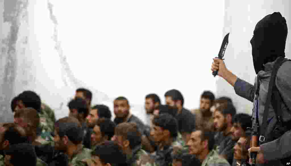 This undated image posted on Wednesday, Aug. 27, 2014 by the Raqqa Media Center, a Syrian opposition group, shows a fighter from the Islamic State armed with a knife and an automatic weapon next to captured Syrian army soldiers and officers, following the battle for the Tabqa air base, Raqqa, Syria. 