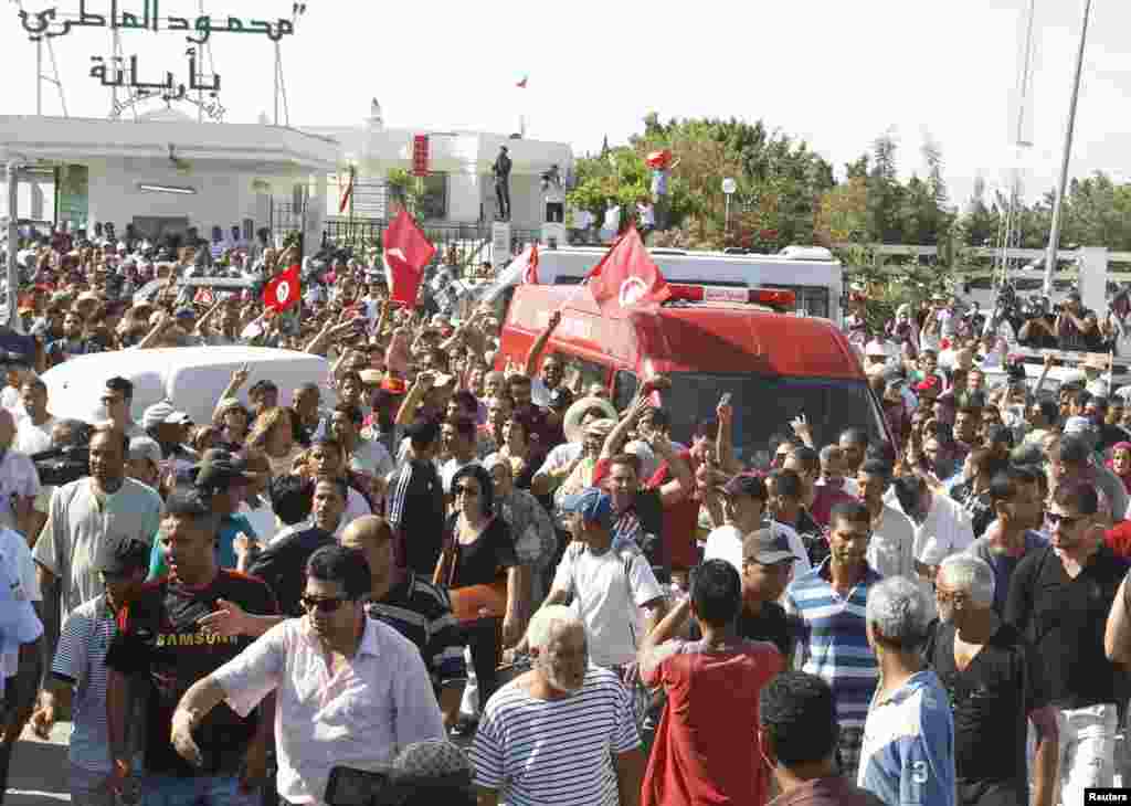 People walk beside the ambulance carrying the body of assassinated Tunisian opposition politician, Mohamed Brahmi, Tunis, July 25, 2013. 